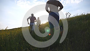 Group of young men running up the green hill over blue sky with sun flare at background. Male athletes is jogging in