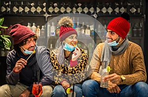 Group of young millennial friends wearing protective face mask celebrating christmas holidays drinking and eating together in the