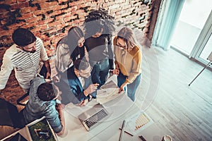 Group of young modern people in smart casual wear having a brainstorm meeting while standing behind the laptop in the creative