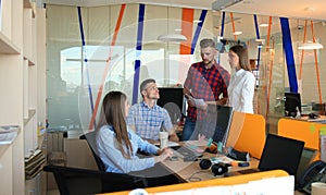 Group of young modern people in smart casual wear having a brainstorm meeting while standing in the creative office.