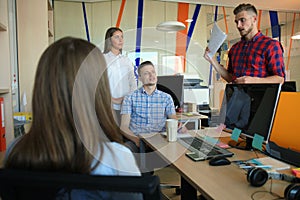 Group of young modern people in smart casual wear having a brainstorm meeting while standing in the creative office.