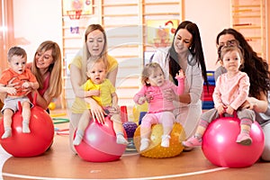 Group of young moms and their babies doing yoga exercises on gymnastic balls at fitness gym