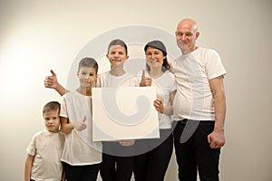 Group of young multi-ethnic beautiful people wearing white shirts, posing together with empty white board. Cheerfull