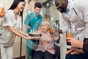 A group of young and old people in a nursing home congratulate an elderly woman on her birthday.