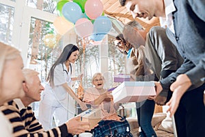 A group of young and old people in a nursing home congratulate an elderly woman on her birthday.