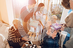 A group of young and old people in a nursing home congratulate an elderly woman on her birthday.