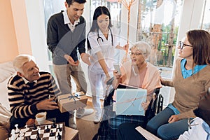 A group of young and old people in a retirement home give an elderly woman a mobile phone.