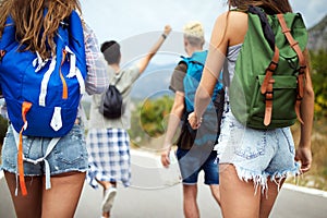 Group of young people with backpacks walking together by the road