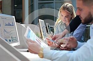 Group of young people in casual wear sitting at the office desk and discussing something while looking at PC together.