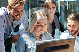 Group of young people in casual wear sitting at the office desk and discussing something while looking at PC together.