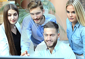 Group of young people in casual wear sitting at the office desk and discussing something while looking at PC together.