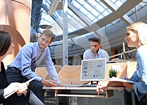 Group of young people in casual wear sitting at the office desk and discussing something while looking at PC together.