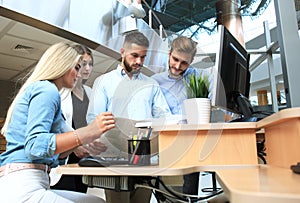 Group of young people in casual wear sitting at the office desk and discussing something while looking at PC together.