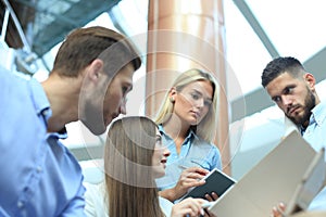 Group of young people in casual wear sitting at the office desk and discussing something while looking at PC together.