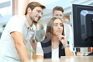 Group of young people in casual wear sitting at the office desk and discussing something while looking at PC together.