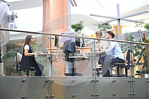 Group of young people in casual wear sitting at the office desk and discussing something while looking at PC together.