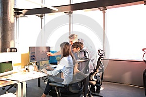 Group of young people in casual wear sitting at the office desk and discussing something while looking at PC together.