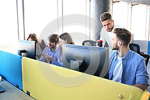 Group of young people in casual wear sitting at the office desk and discussing something while looking at PC together.