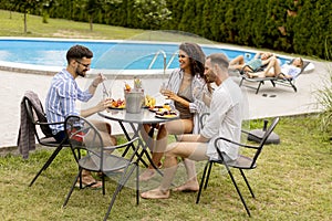 Group of young people cheering with drinks and eating fruits by the pool in the garden