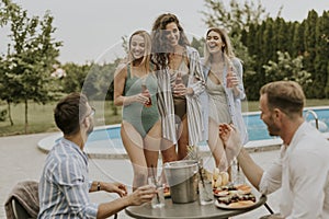 Group of young people cheering with drinks and eating fruits by the pool in the garden