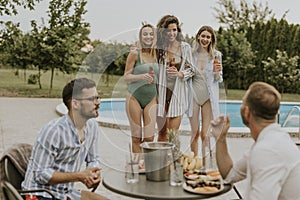 Group of young people cheering with drinks and eating fruits by the pool in the garden