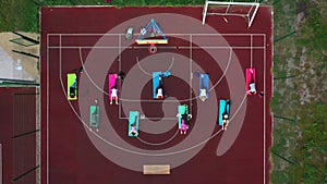 Group of young people doing workout on the red sportground. Top aerial view.