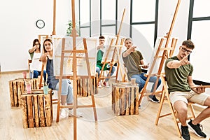 Group of young people drawing at art studio pointing with finger to the camera and to you, confident gesture looking serious