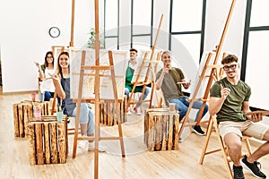 Group of young people drawing at art studio smiling happy pointing with hand and finger to the side