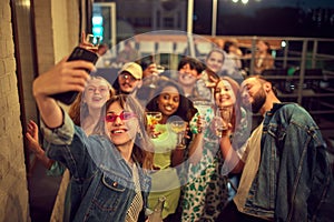 Group of young people, friends meeting on rooftop in evening, having good time together, taking selfie