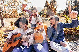 Young people hangout in the park.They sitting on bench ,singing and playing guitar