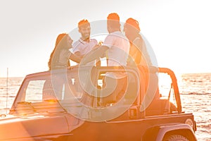 Group of young people having fun in convertible car at the beach at sunset.