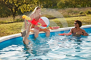 Group of young people having fun in swimming pool, playing with water guns and inflatable ball