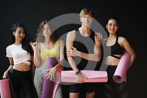 Group of young  people holding yoga mats While leaning against the black wall in the gym