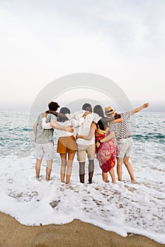 Group of young people hugging each other and enjoying sunset at beach
