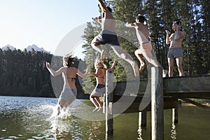 Group Of Young People Jumping From Jetty Into Lake