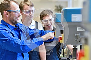 Group of young people in mechanical vocational training with teacher at drilling machine photo