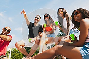 Group of young people, men and women resting on the beach, drinking cool drinks, having fun, sunbathing