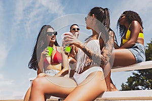 Group of young people, men and women resting on the beach, drinking cool drinks, having fun, sunbathing