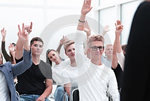 Group of young people raising their hands to ask a question.