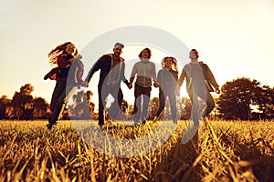 A group of young people running through the grass in the park at sunset.