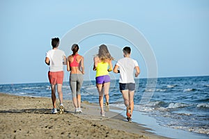 Group of young people running in the sand on the shore of a beach by the sea at sunset during a sunny summer holiday vacation