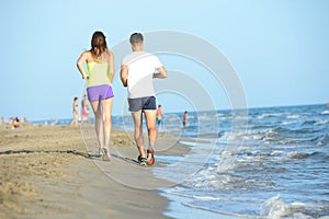 Group of young people running in the sand on the shore of a beach by the sea at sunset during a sunny summer holiday vacation