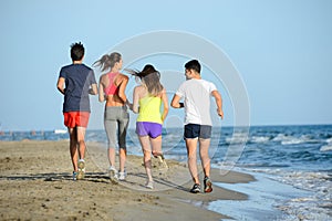 Group of young people running in the sand on the shore of a beach by the sea at sunset during a sunny summer holiday vacation