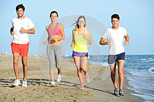 Group of young people running in the sand on the shore of a beach by the sea at sunset during a sunny summer holiday vacation