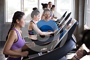 group of young people running on treadmills in sport gym .fitness woman runner on running machine with trainer man in morning time