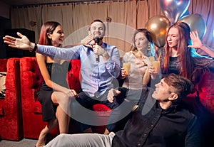 Group of young people singing into microphone at party,celebrating birthday, karaoke