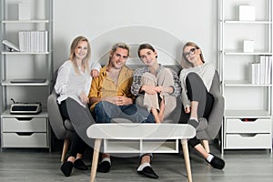 Group of young people sitting on sofa and talking at home. Cheerful young people in casual wear laughing sitting on