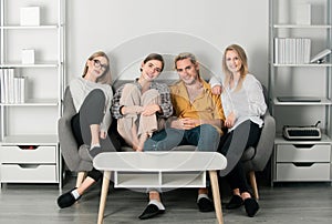 Group of young people sitting on sofa and talking at home. Cheerful young people in casual wear laughing sitting on