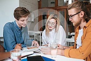 Group of young people sitting at the table and working together in office. Pretty girl and two boys happily discussing