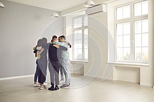 Group of young people standing in circle in office space, hugging each other and talking